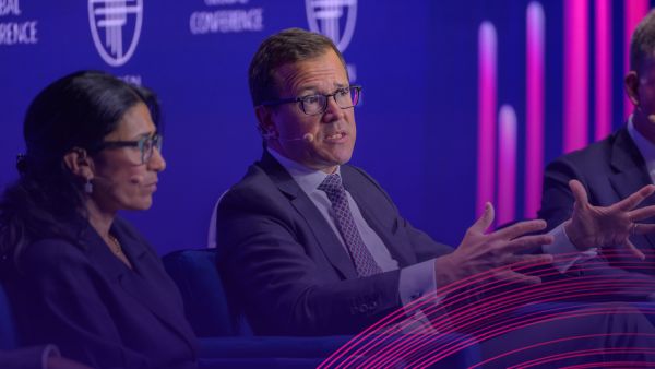 Panelists speak during the "Credit Outlook" session at Global Conference 2025. A man in a suit gestures while speaking, seated beside other panelists on stage with microphones and a blue backdrop featuring the Milken Institute logo.